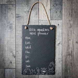 Slate meal planner board with 'little monsters meal planner' on a wooden wall